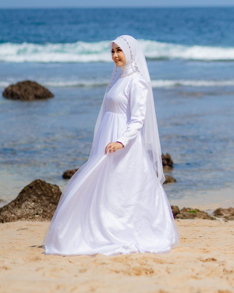 Potret Tita di tepi pantai, memegang ujung gaun