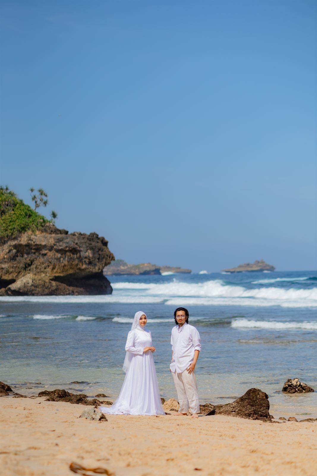 Shovian dan Tita berdiri di pantai dengan tebing di kejauhan